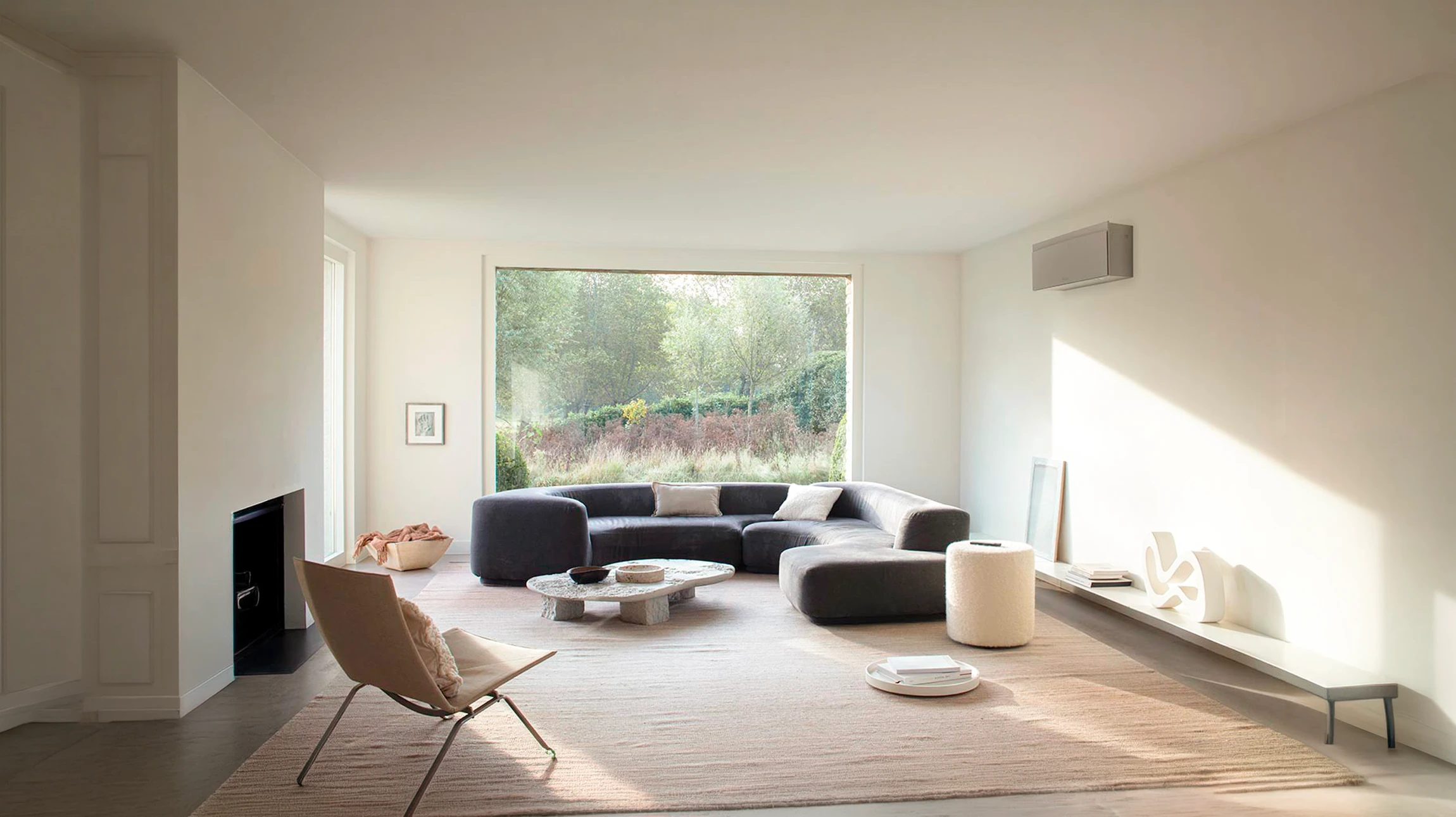 Salon minimaliste lumineux avec canapé d'angle modulaire en tissu anthracite, fauteuil lounge scandinave en cuir beige, table basse en pierre naturelle