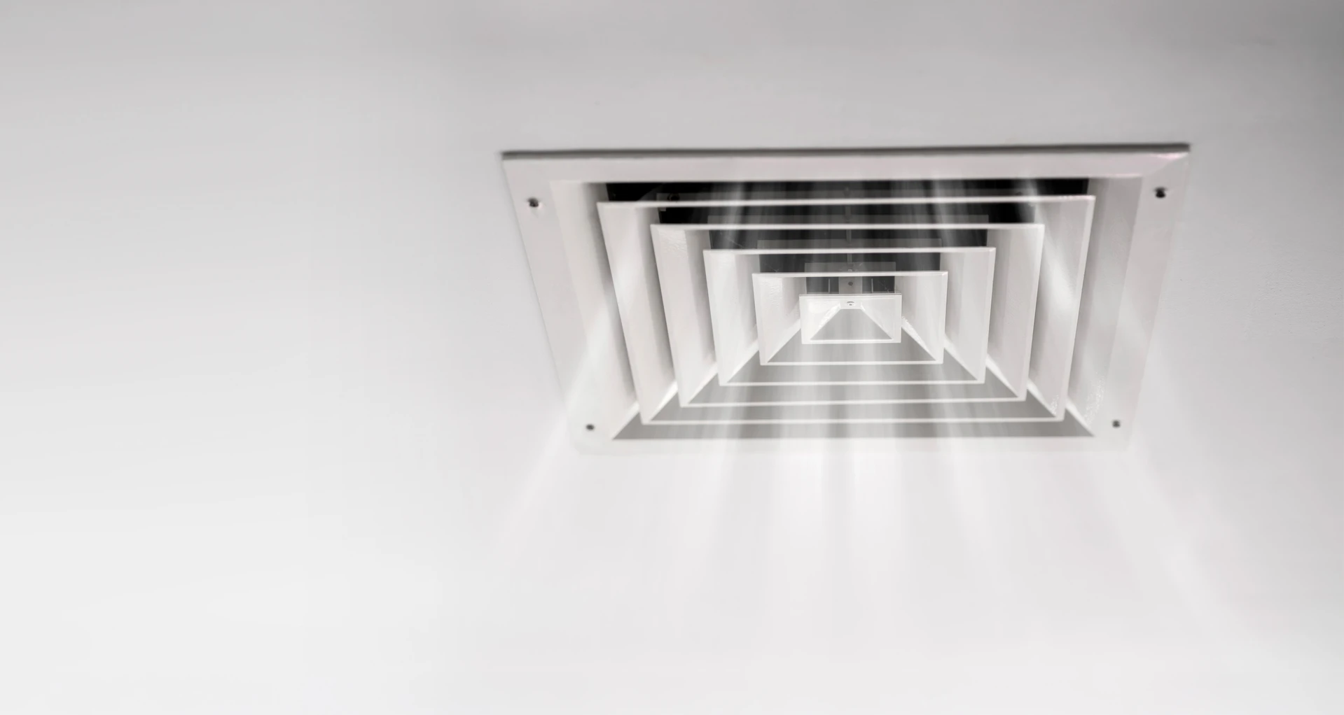 Photographie d'un technicien professionnel en tenue de travail installant une VMC (bouche d'extraction) dans une cuisine ou une salle de bain résidentielle, montrant le boîtier de ventilation fixé au mur ou au plafond avec les conduits apparents ou en cours de connexion. L'artisan doit être concentré sur son travail, avec des outils visibles, illustrant une installation complète et professionnelle d'un système de ventilation mécanique contrôlée.