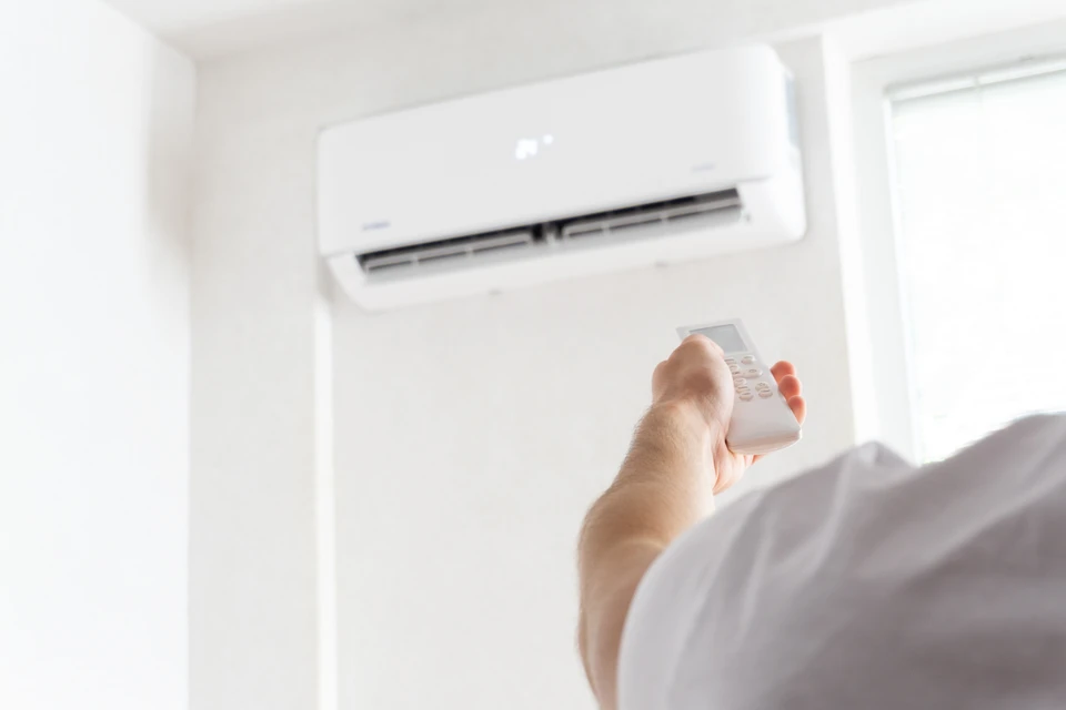 Homme en chemise grise et gants bleus effectuant la maintenance sur l'unité de climatisation dans l'environnement intérieur moderne pour une efficacité de refroidissement optimale et une amélioration de la qualité de l'air pur